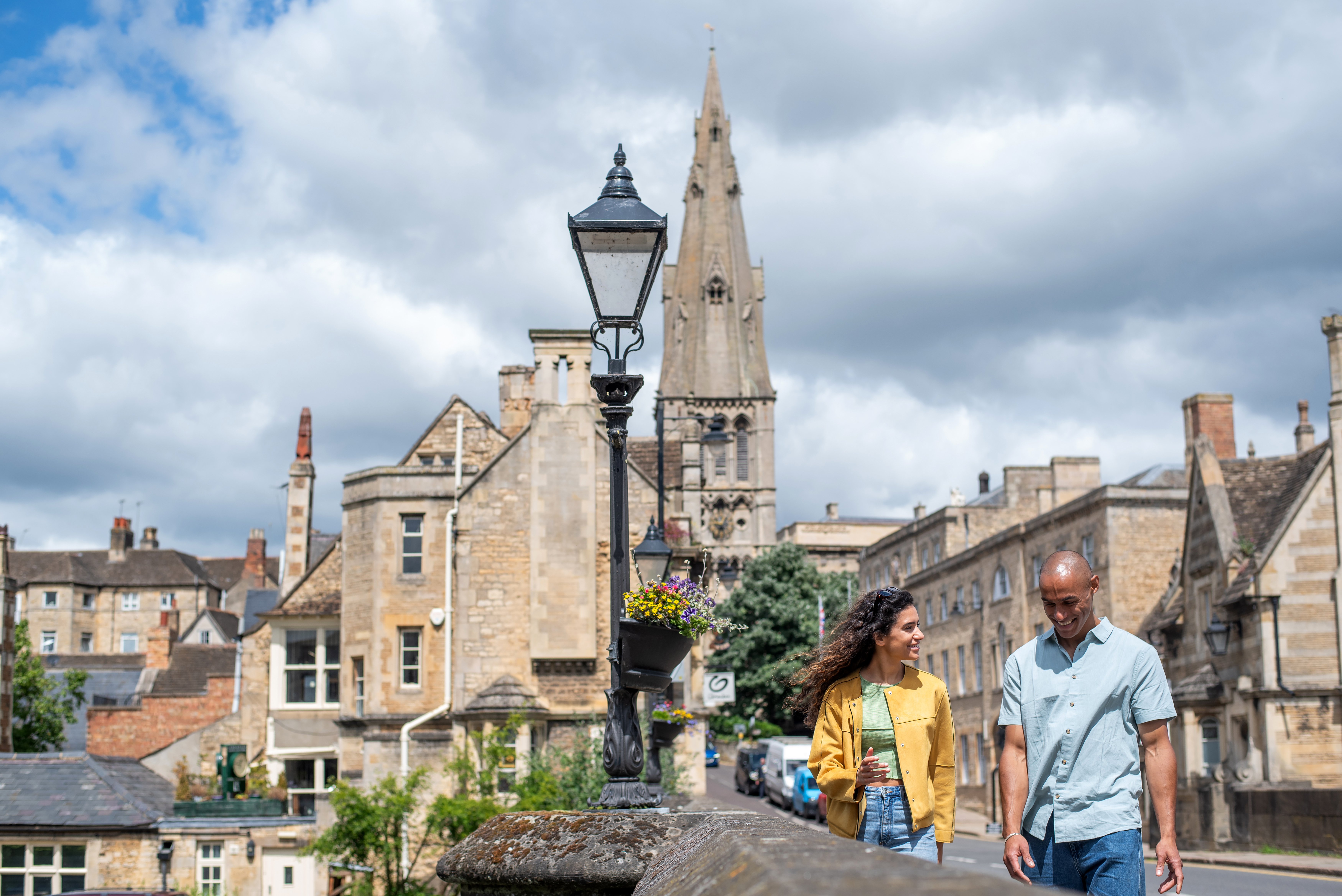 A man and a woman walk through a stone built village with a church