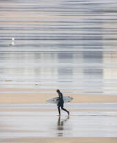 Surfer walking out of the sea holding a surfboard and wearing a wetsuit