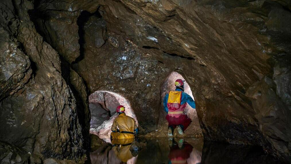 A part-flooded natural cave chamber with two lead miners' tunnels blasted at the far end in Speedwell Cavern in Castleton, Derbyshire.