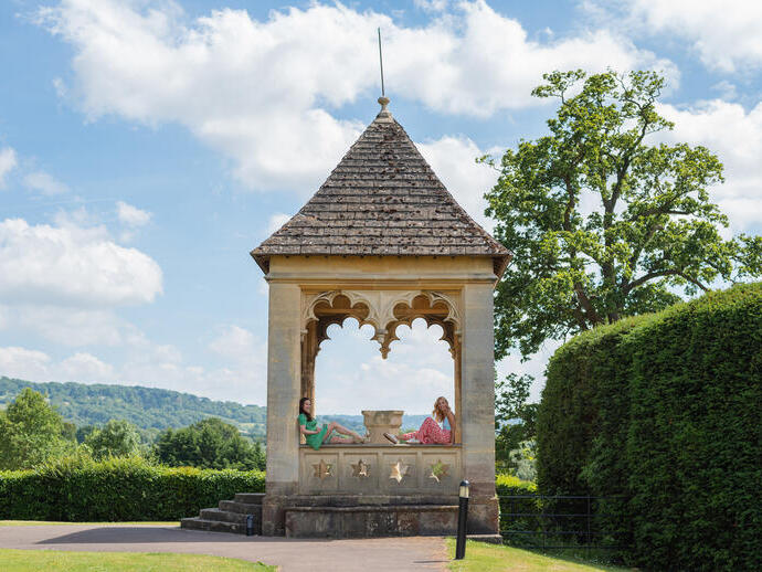 Two women sit on a monument in gardens