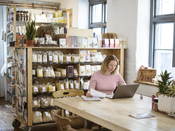Woman in early 40s using laptop at a communal table in a health food shop and cafe