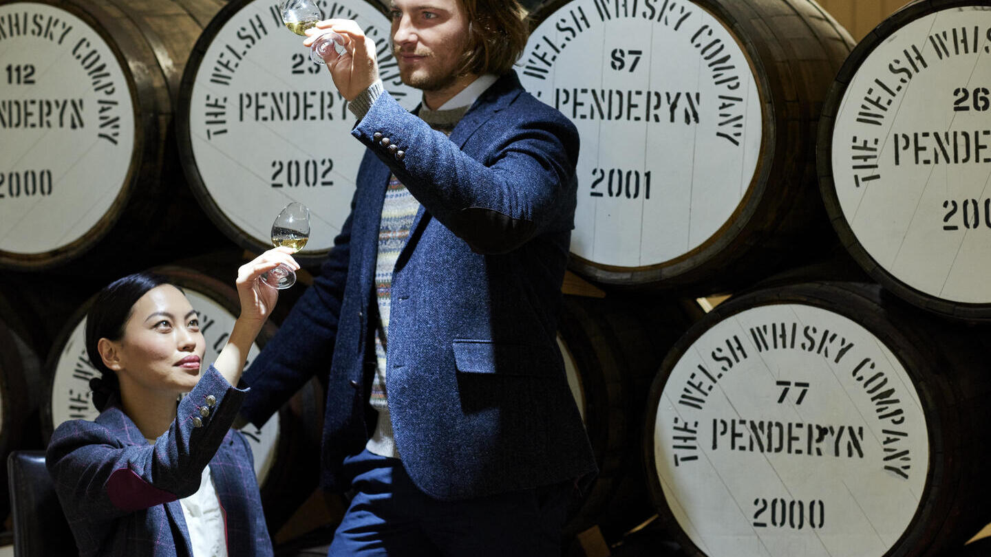 A man and a woman standing next to a stack of oak barrels