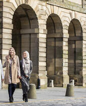Three women walking by stone arches in a city