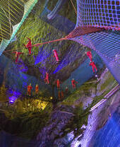 Group of people bouncing on net trampolines suspended in deep caverns