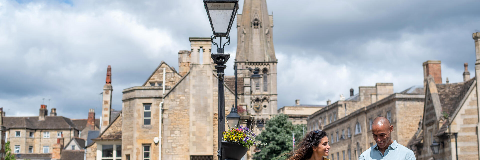 A man and a woman walk through a stone built village with a church