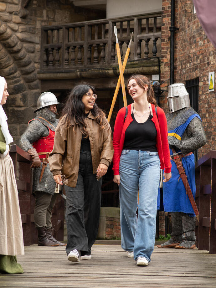 Two women walk passed people dressed in medieval costume at a castle