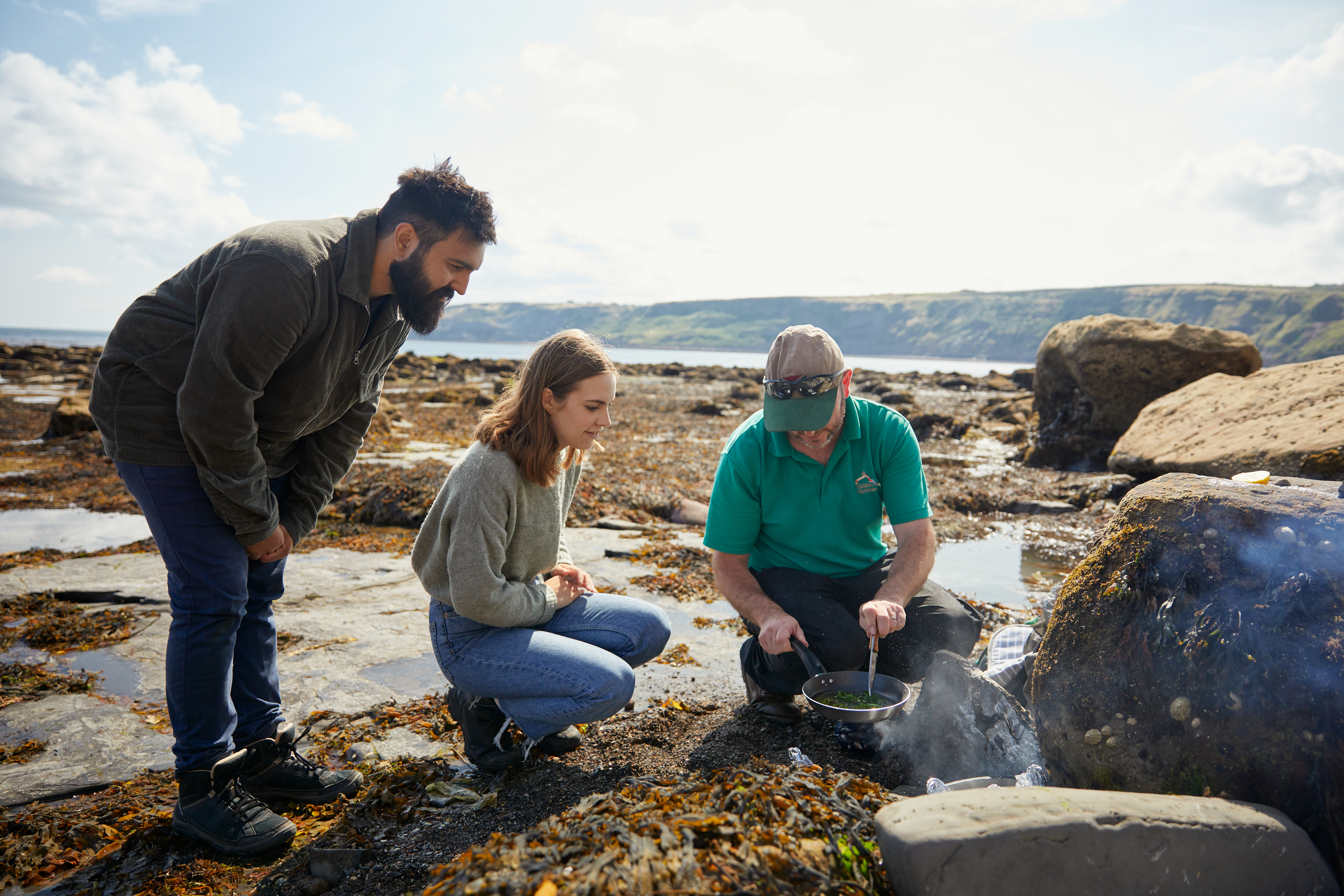 Trois personnes parmi les rochers au bord de la mer, l'une d'elles est en train de cuisiner