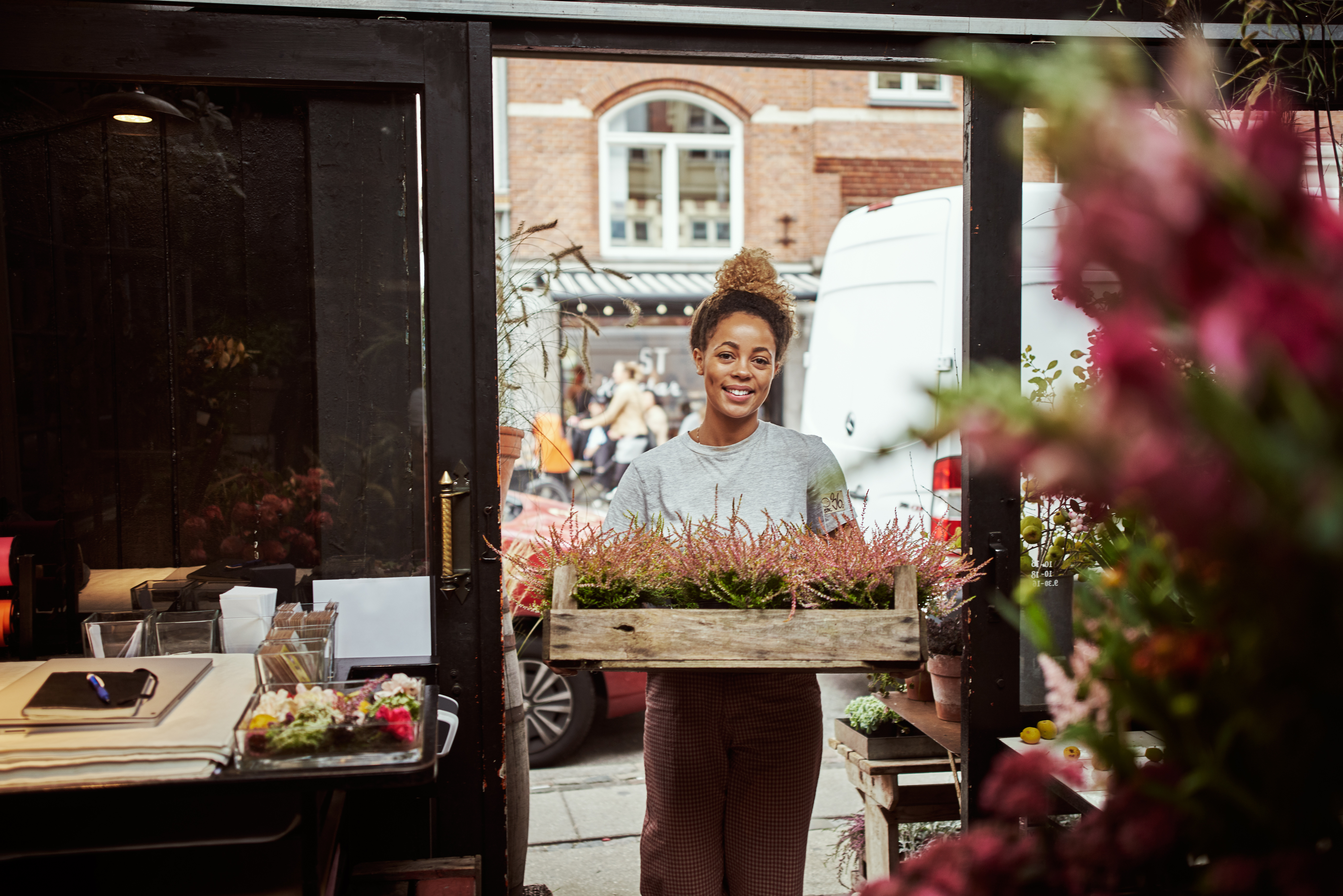 Young woman entering her flower shop carrying a tray of heather plants