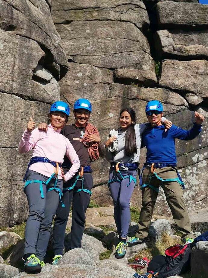 Una squadra di quattro persone in piedi davanti a una parete rocciosa con indosso l'attrezzatura da arrampicata