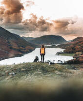Woman standing with two dogs looking down at a lake in a valley