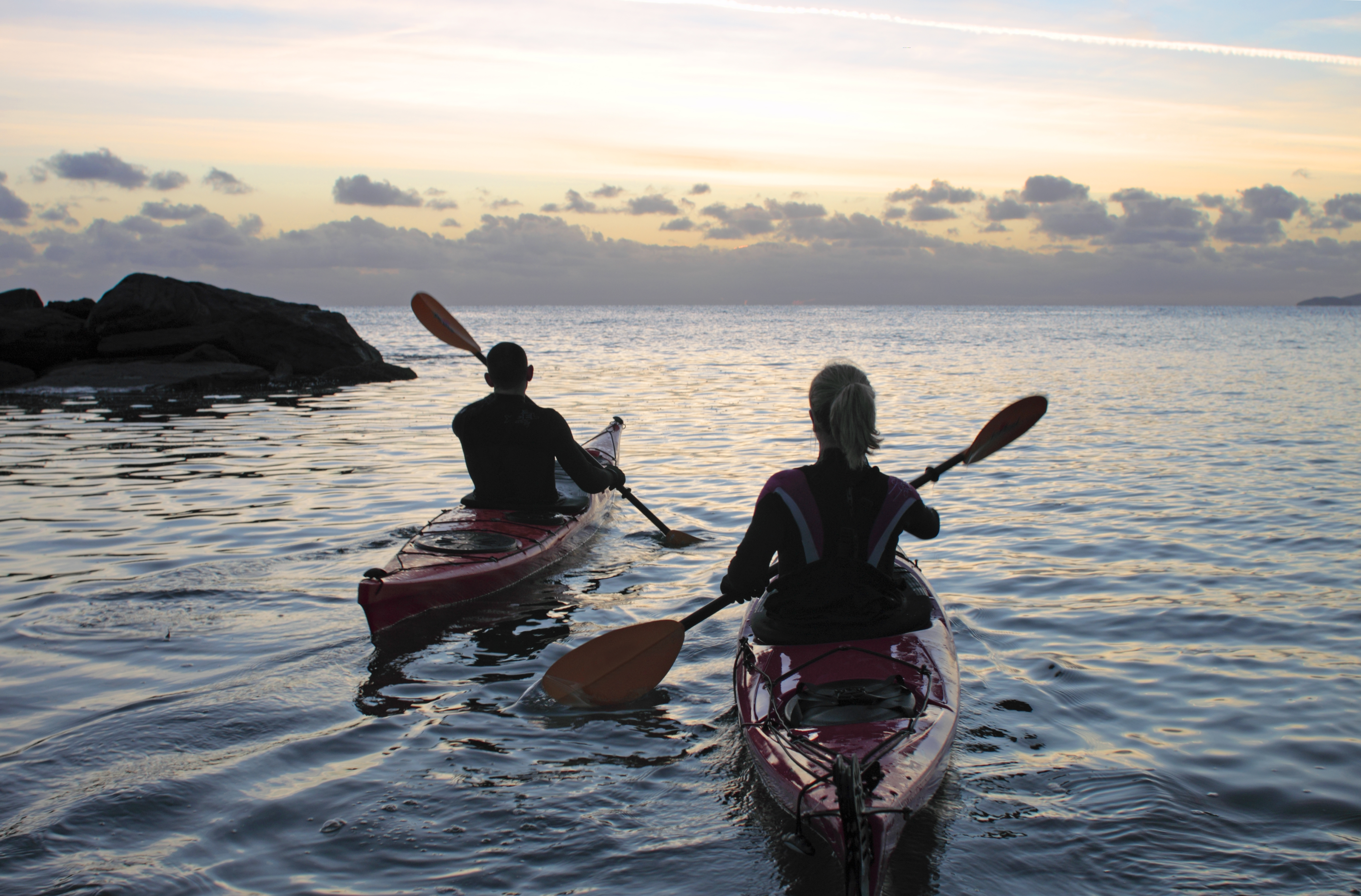 A couple kayaking off the coast of a rocky coastline.