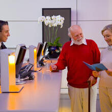 Couple, one with walking stick at a check-in desk of a hotel