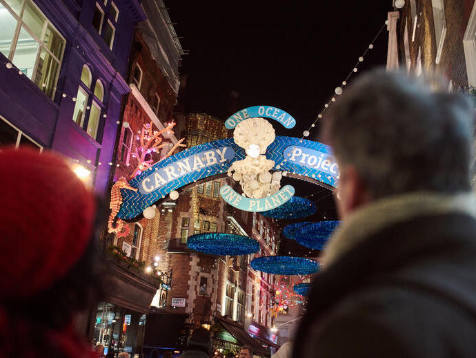 زوجان ينظران إلى أضواء الشوارع وزينة عيد الميلاد ولافتة شارع كبيرة