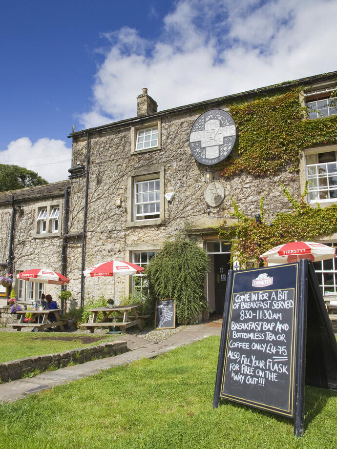 Tables with umbrellas, chairs and signage on grass outside pub