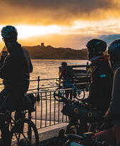 Un grupo de ciclistas tomando una foto de la puesta de sol en la costa