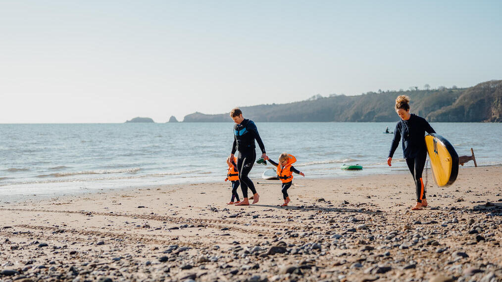 Une famille se promenant sur la plage, l'homme est accompagné de deux jeunes enfants et la femme tient une planche de surf à Saundersfoot Beach