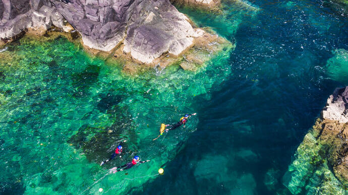 People coasteering along the ocean edge by rocky cliffs.