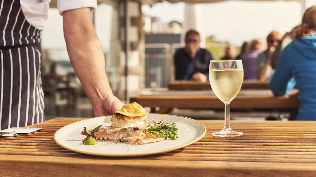 Waiter placing plate of food on table beside glass of wine