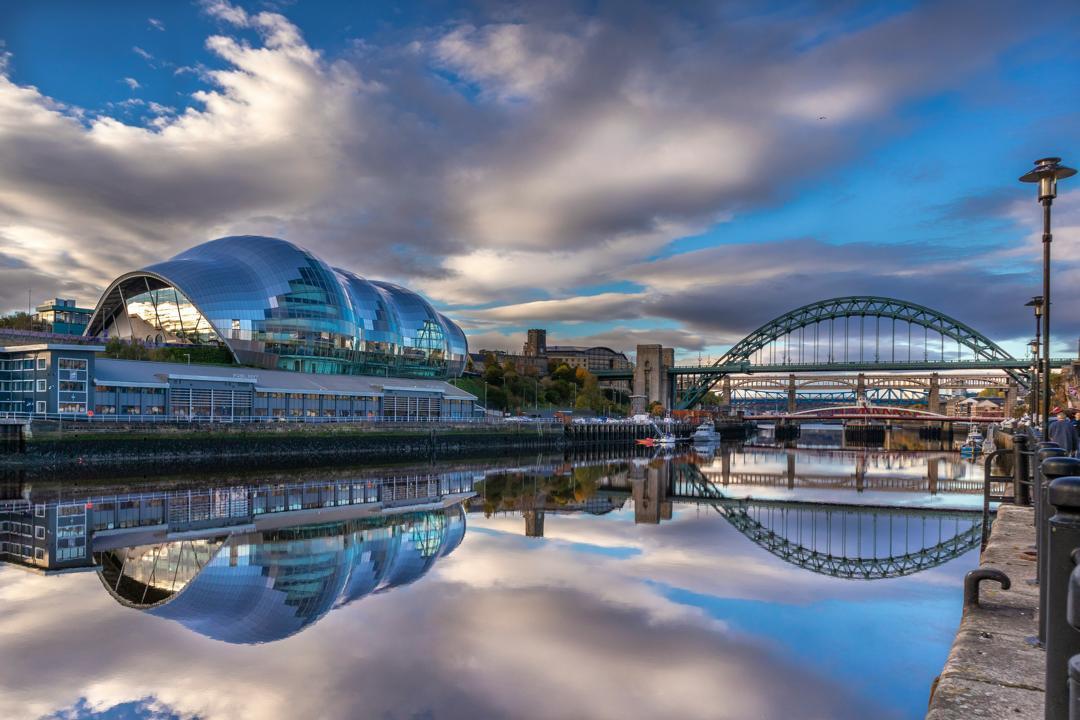 A modern glass international music centre along a calm river next to an arched bridge.