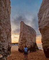 Man standing on a beach looking up free standing rock formations