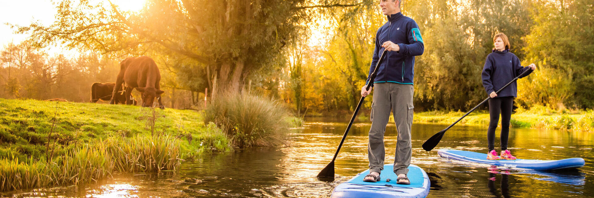 Two people paddleboarding down the River Bure