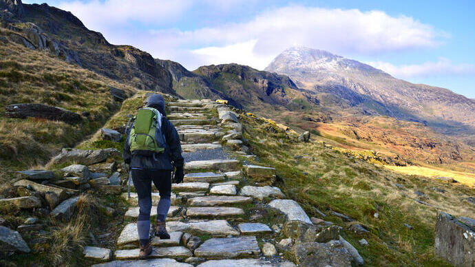 Excursionista subiendo por un camino empedrado de montaña a través de una cordillera árida.