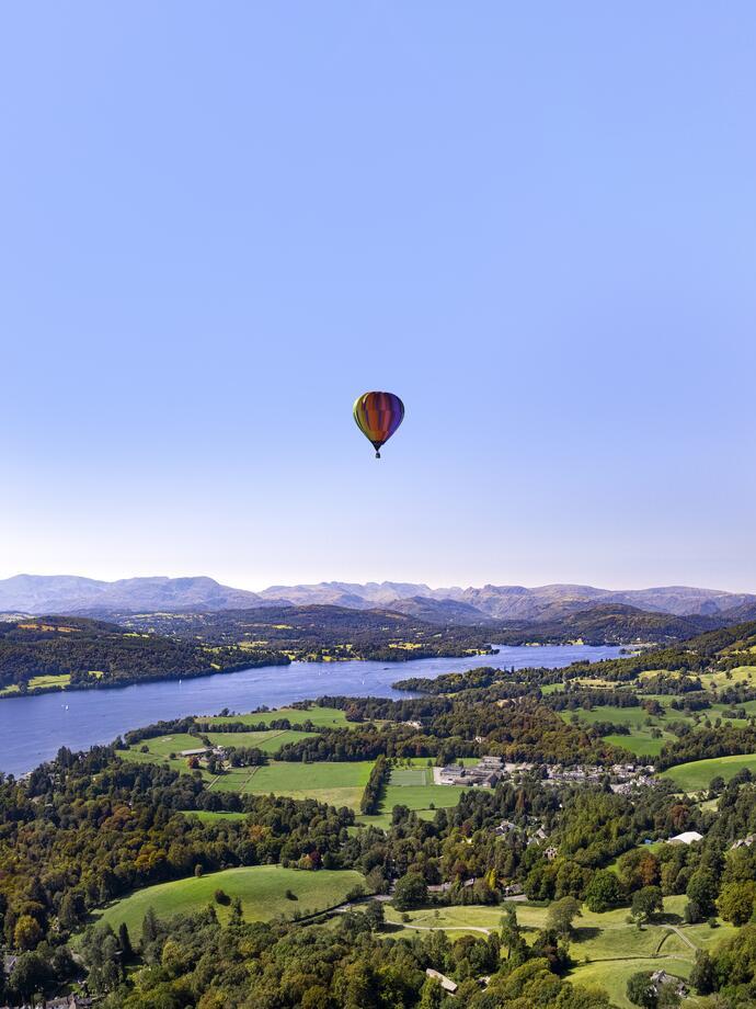 Hot air balloon in clear skies over green countryside fields