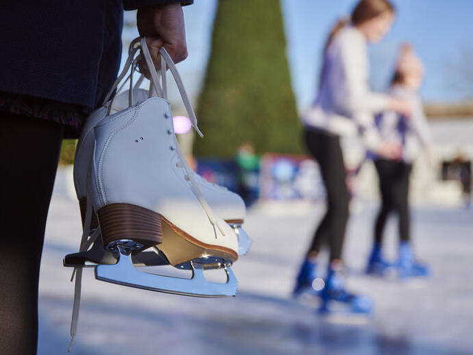 Hands holding a pair of white ice skates by the laces