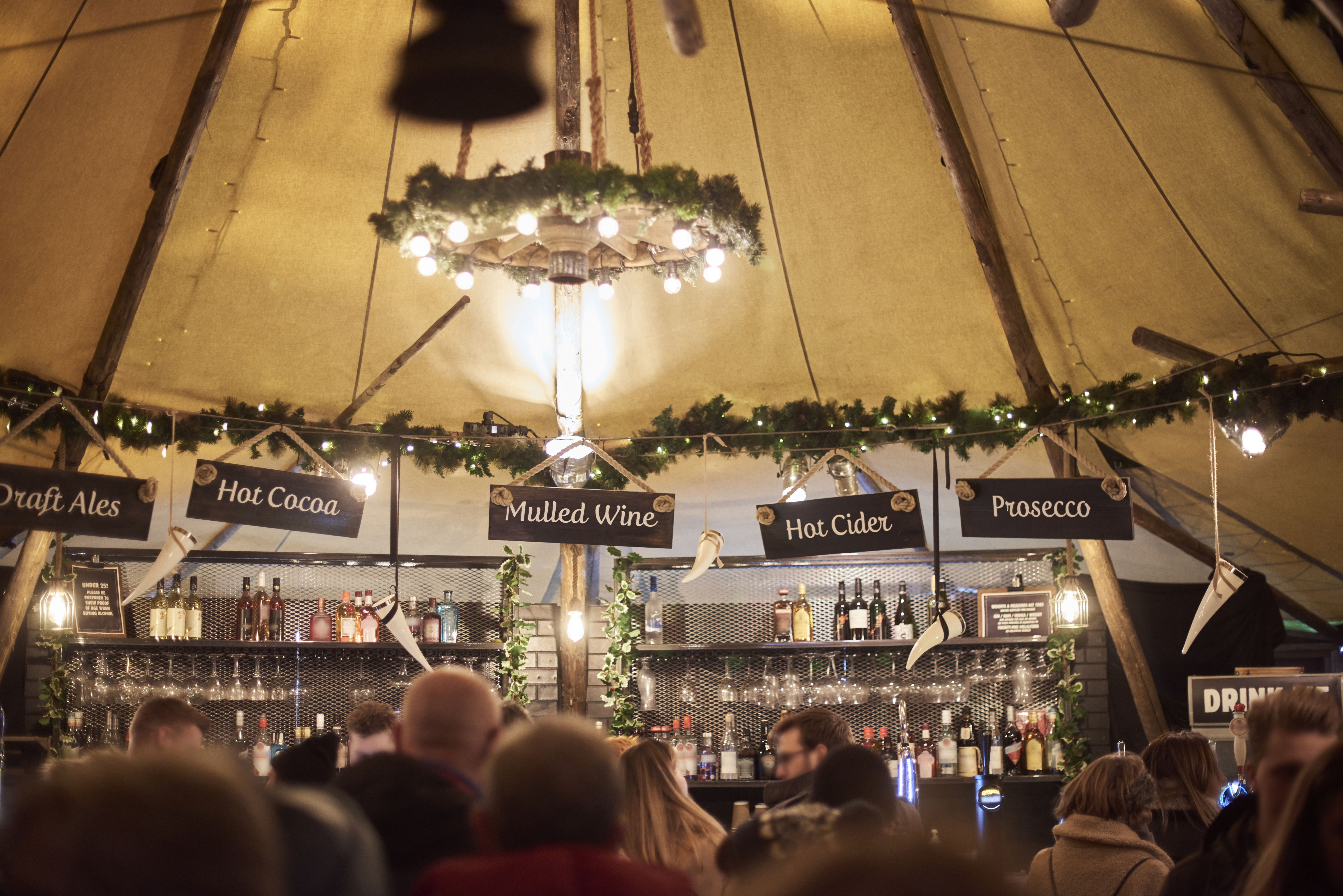 Des gens devant un bar sous un chapiteau, éclairé par des guirlandes lumineuses