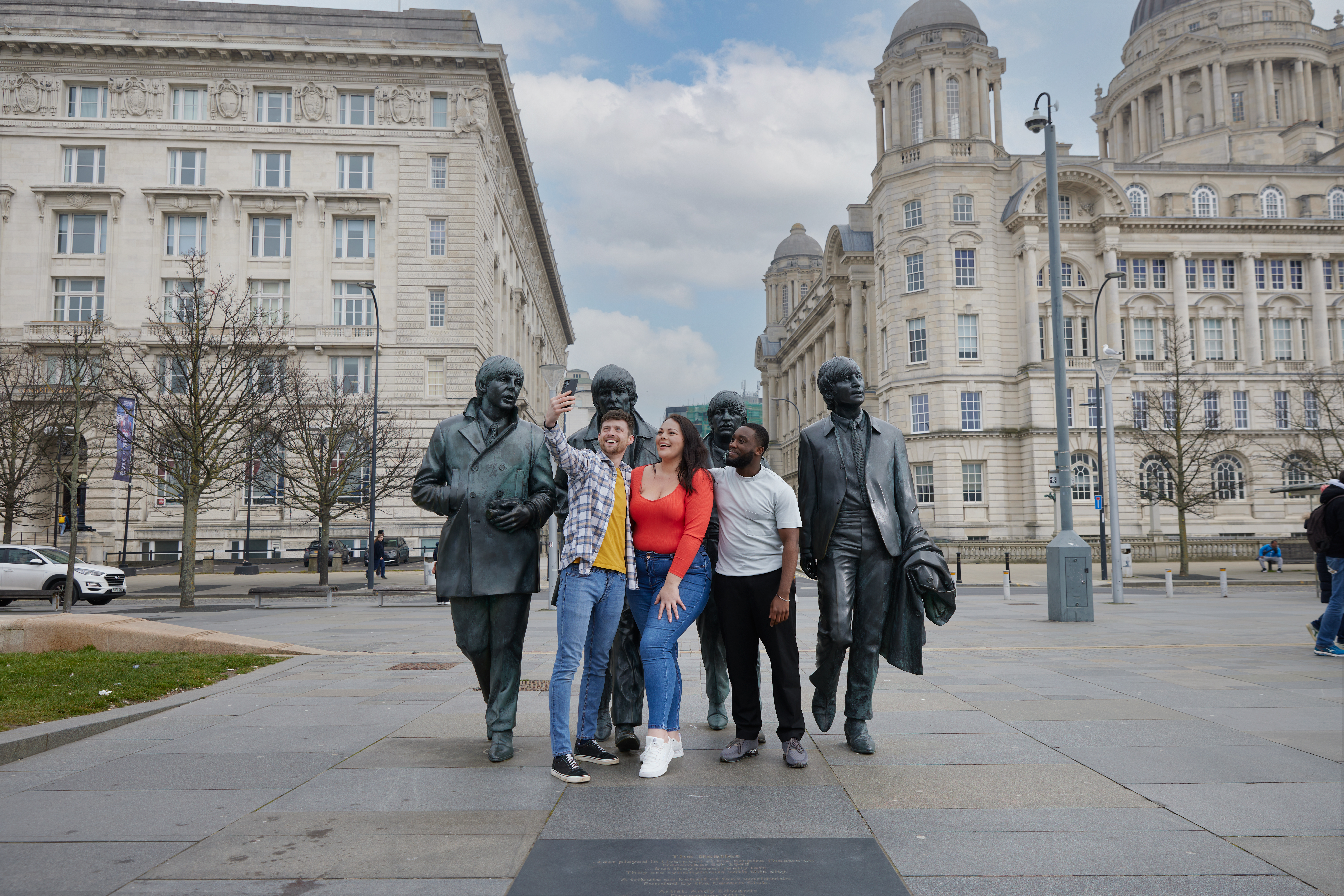 Eine Gruppe von Freunden, zwei Männer und eine Frau, machen ein Selfie vor einer Statue im Stadtzentrum.