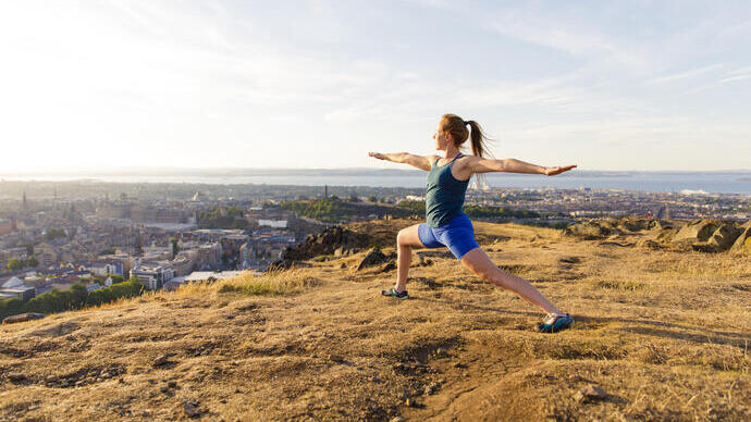 Young woman doing yoga on a hill overlooking a city