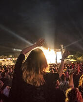 Mujer entre la multitud en un concierto de música con los brazos en alto viendo una actuación