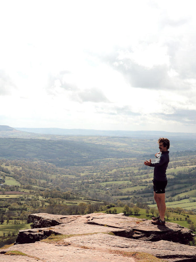 A man standing on the peak of a hill with landscape views of the countryside