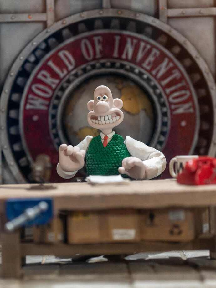 Figurine de Wallace assis à un bureau, avec une pancarte indiquant « World of Invention » (Le monde de l'invention) en arrière-plan.