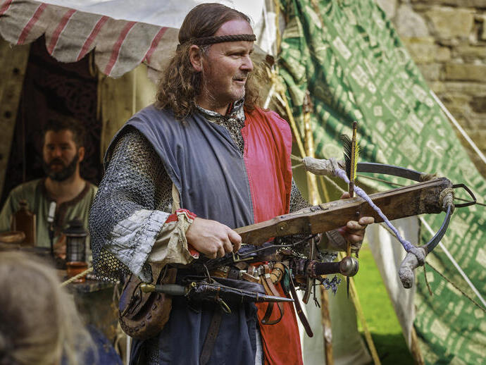 A crossbow actor in costume by a castle showing people how it used to work.