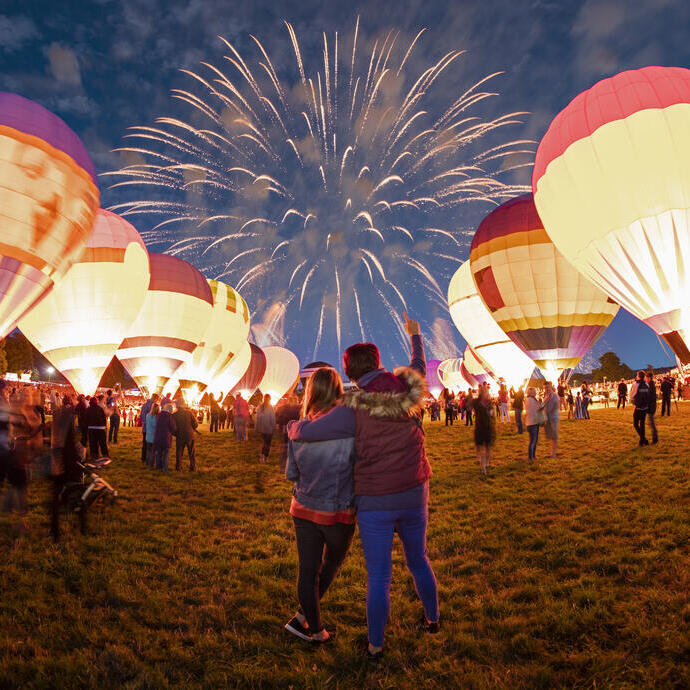 Couple watching grounded hot air balloons and fireworks in the night sky