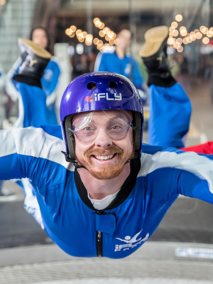 Una persona che prova l'esperienza di paracadutismo indoor iFLY con una folla di persone che guarda dietro