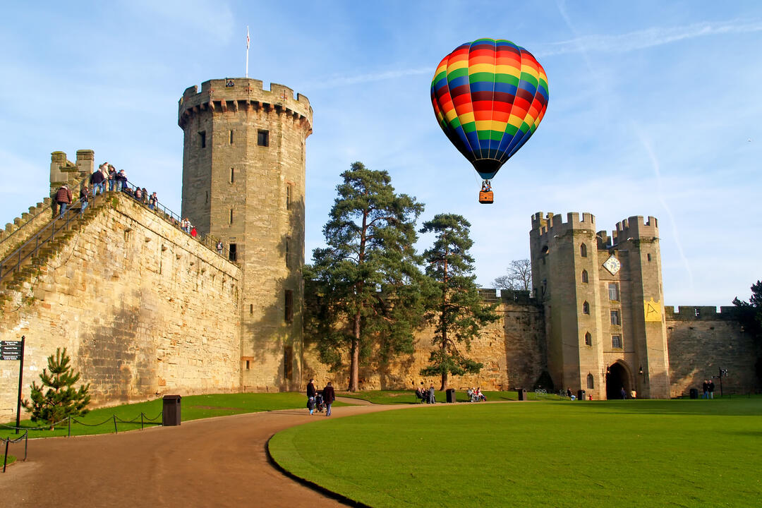 A hot air balloon floats over a castle and its manicured grounds.