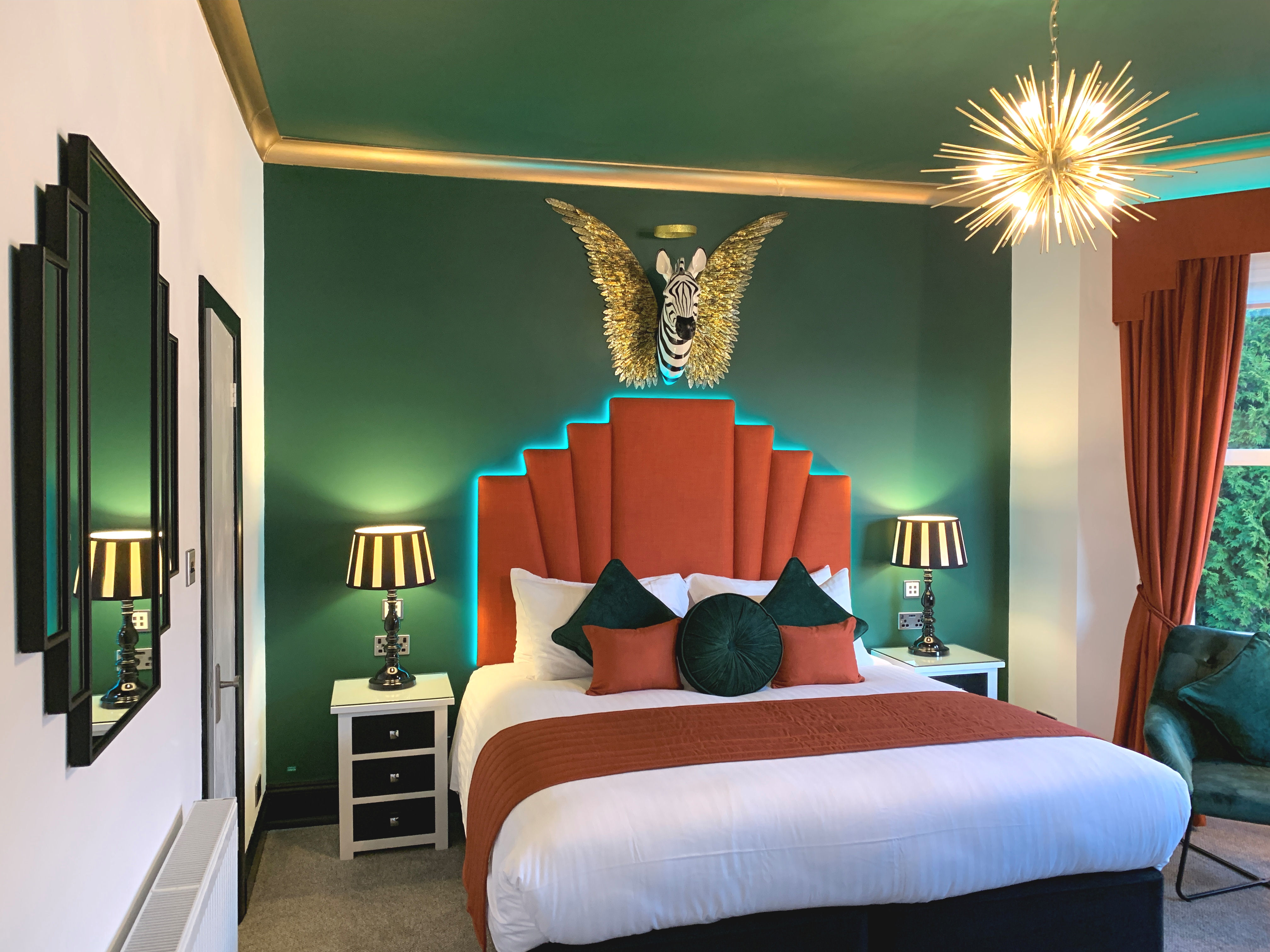 View of a bedroom with a spiky light fitting and the head of a zebra in the centre of a pair of gold wings hung above the bed.