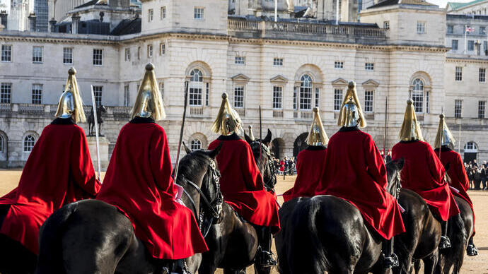 Männer in zeremonieller Uniform reiten auf Pferden in Richtung eines großen historischen Gebäudes und eines Riesenrads