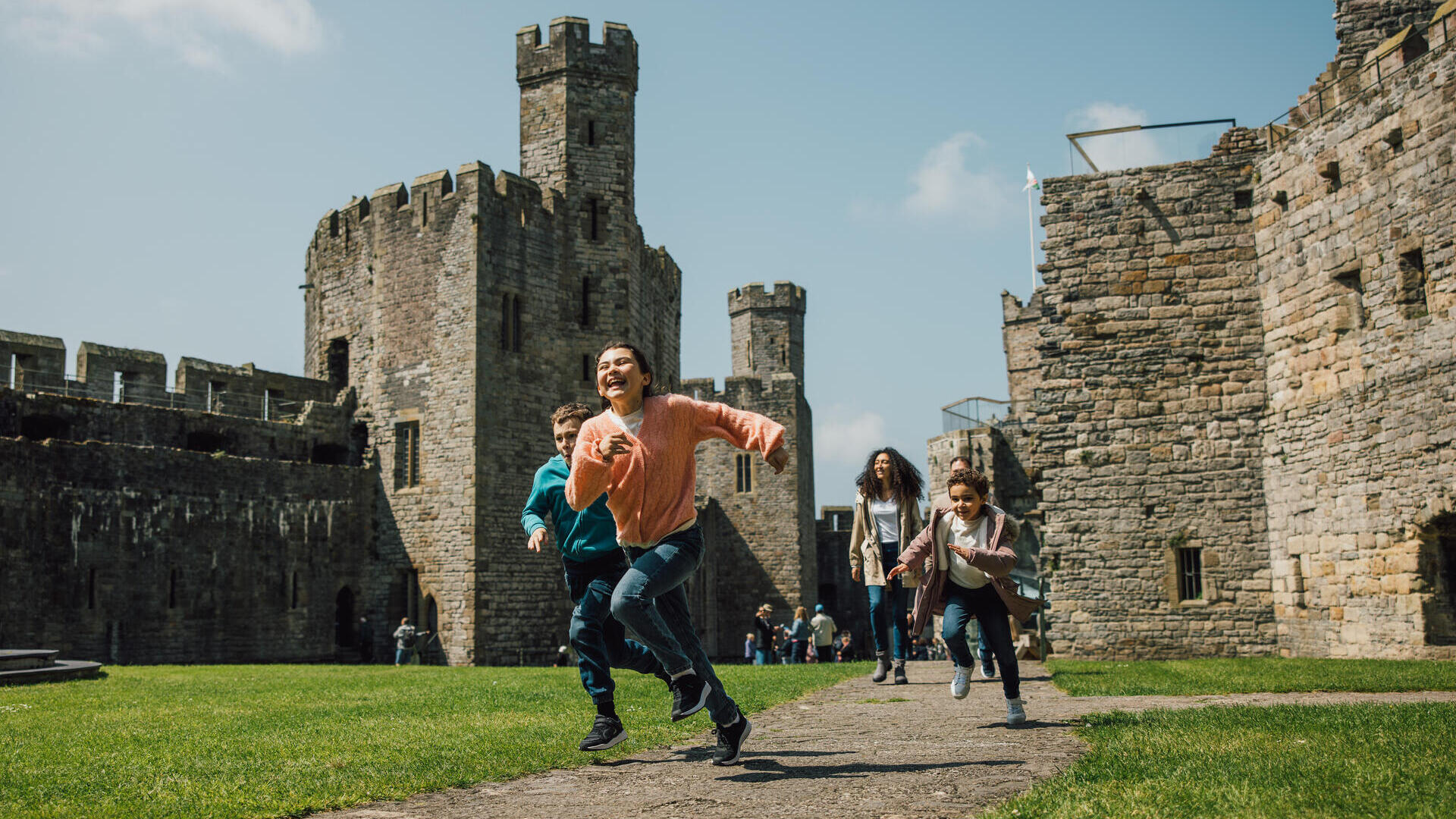 Children running and laughing at a historic stone castle on a sunny day.