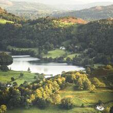 Two people sat on the edge of a fell looking over a green valley with a lake at the bottom
