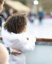 Mother and daughter watching people ice skating on ice rink.