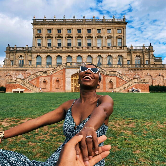 Woman laughing sitting on the grass in front of a stately home