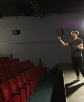 An actor rehearses his lines on a spotlit stage in a small community theatre.