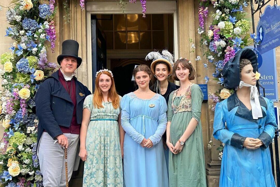 A group of people posing in period Victorian costume under a floral archway.