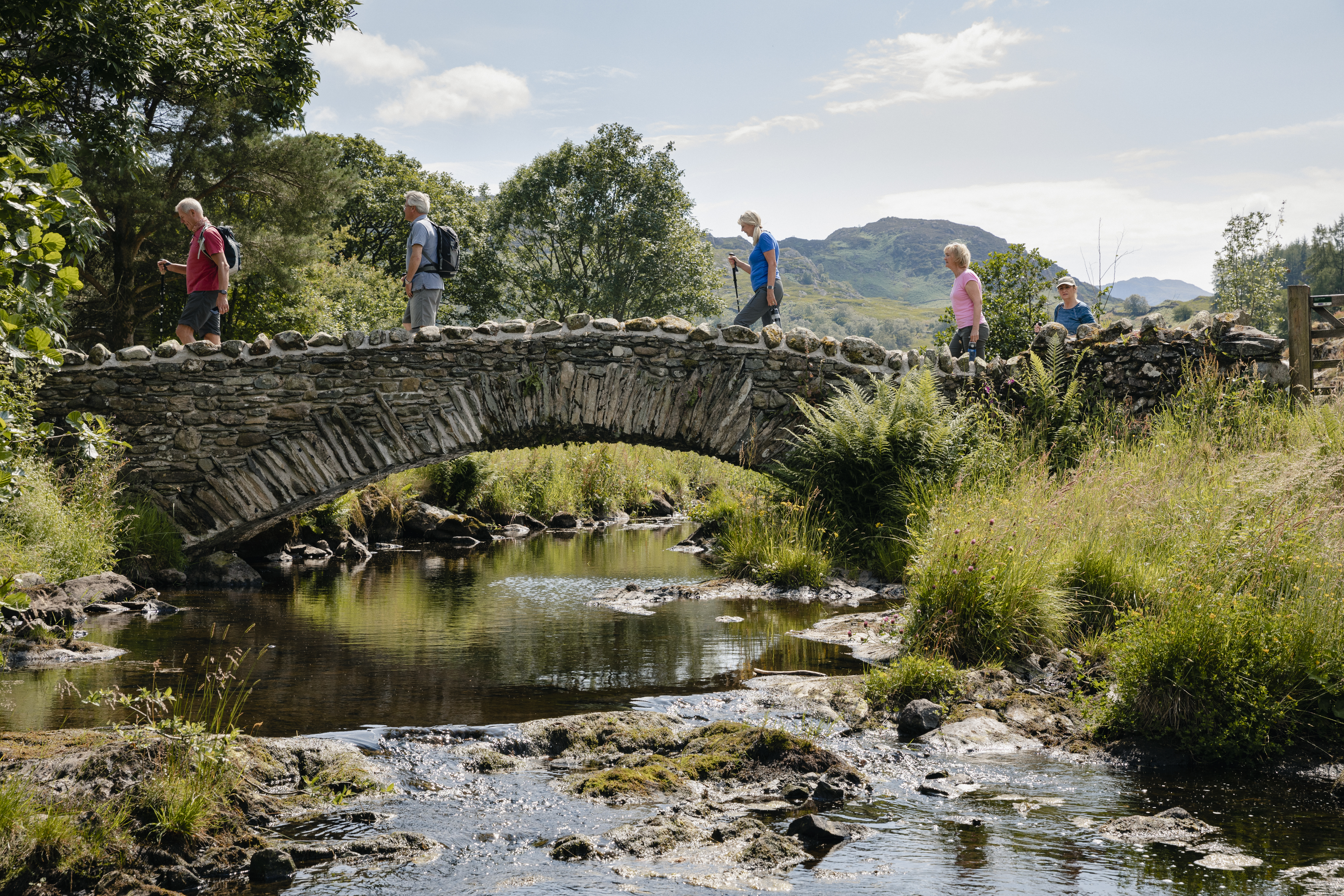 Group of friends crossing bridge over a running stream.