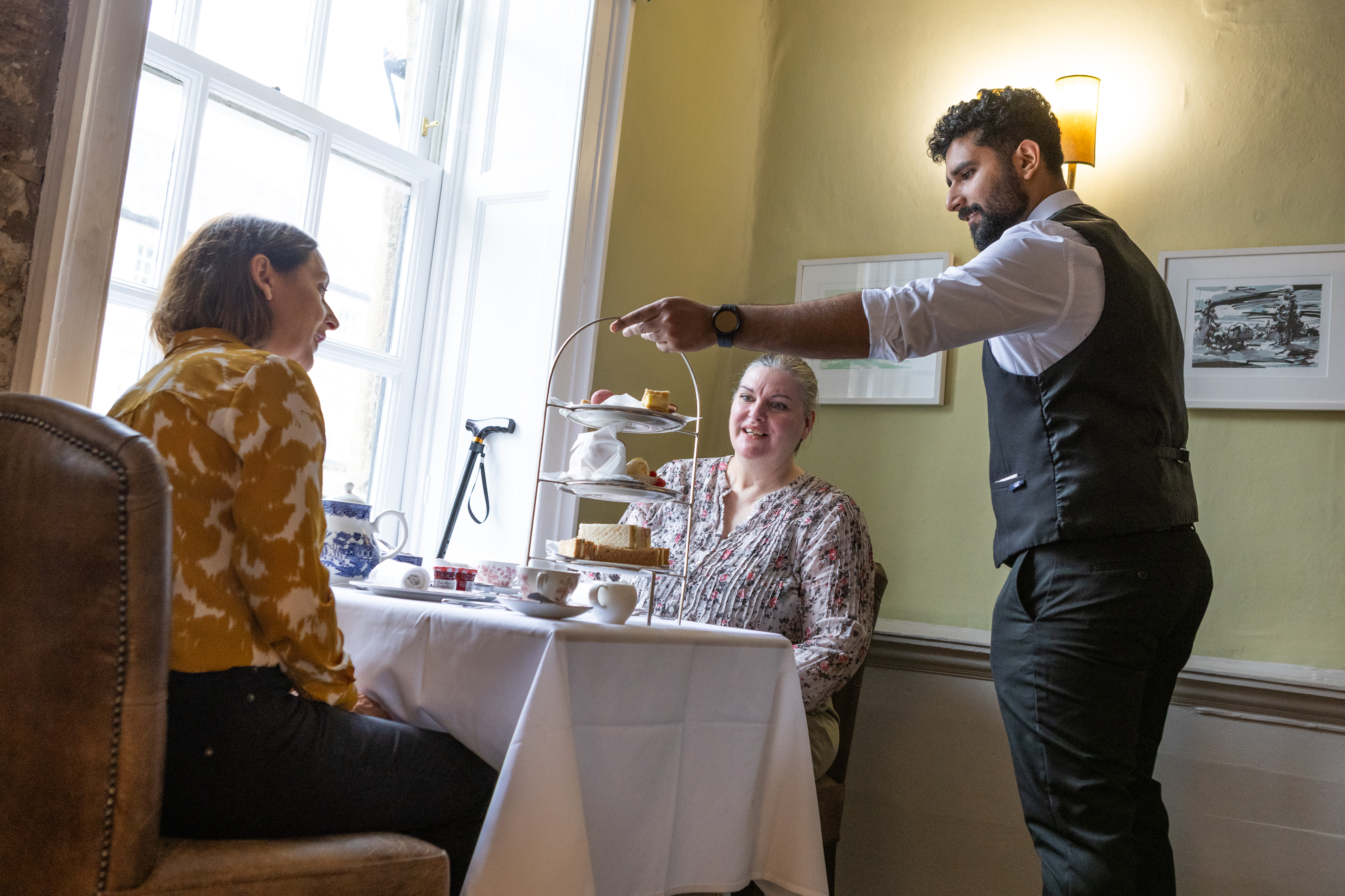 Two women being served afternoon tea by a waiter.