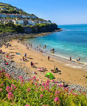 People on a sandy beach in a cove with houses on the cliff behind
