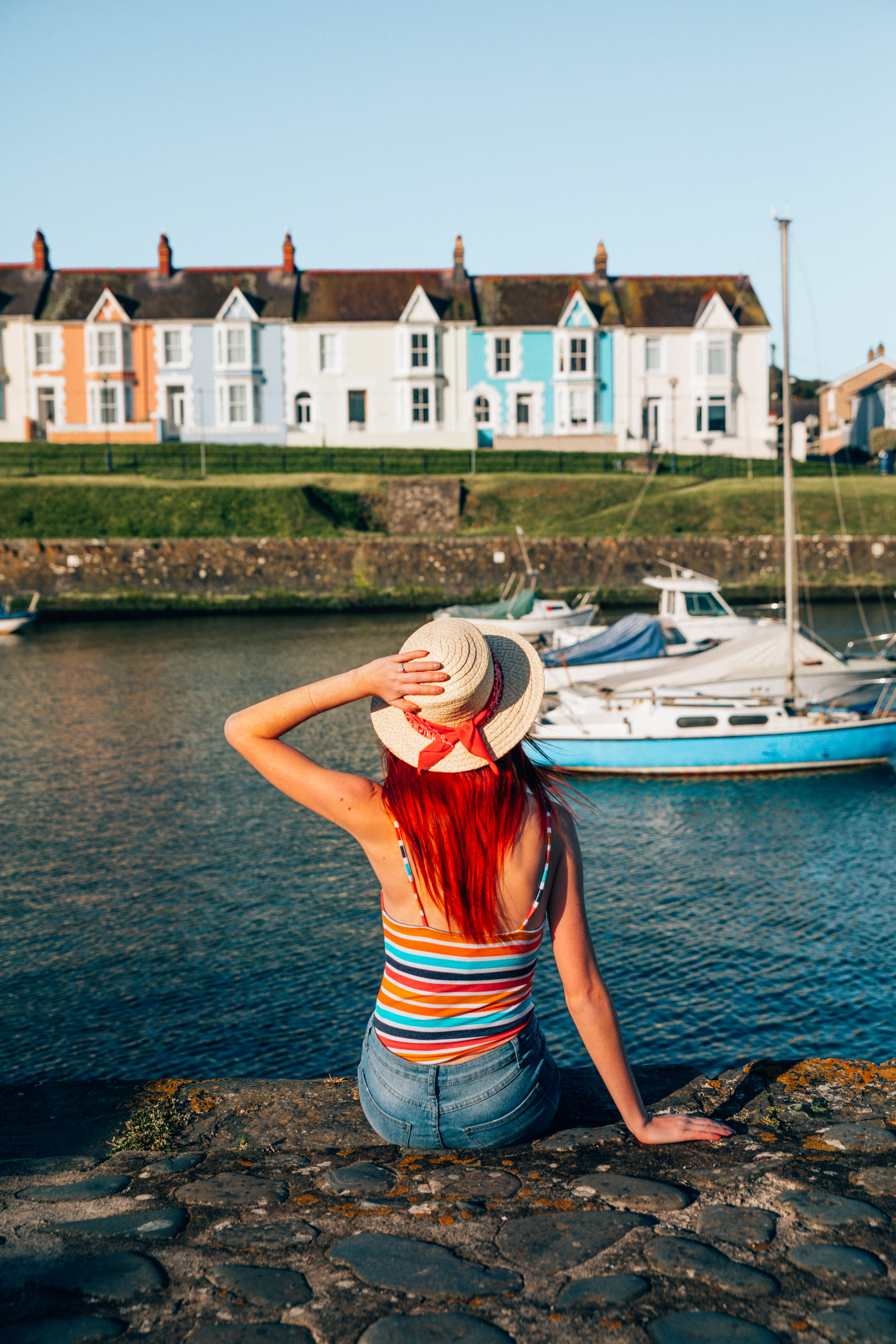 Woman sitting on the wall of a harbour looking at the boats